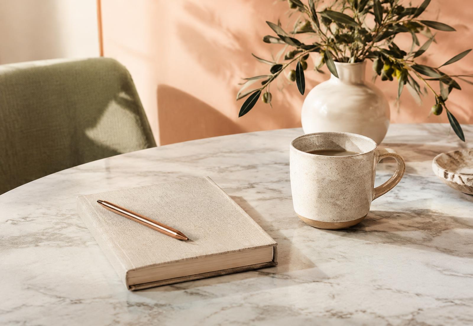 Journal, pen and coffee mug on a marble table